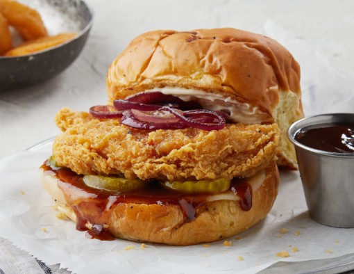 BBQ Chicken Sandwich with a side of onion rings and BBQ sauce on parchment paper