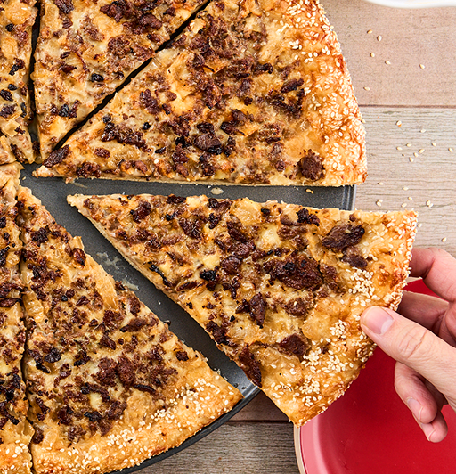 Philly Cheesesteak Pizza with a hand removing a slice to put on a plate. 