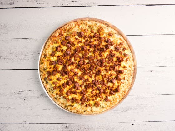 A whole pizza with melted cheese and crumbled sausage on a white wooden background