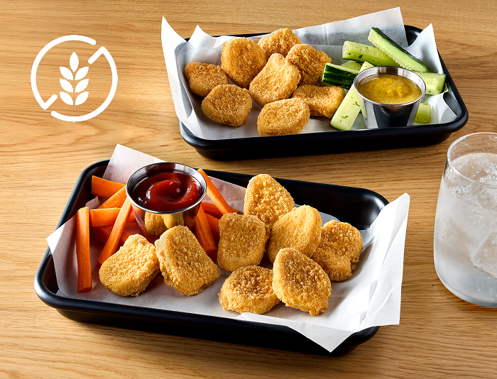 Gluten-free breaded chicken nuggets served in trays with carrot sticks, cucumber spears, dipping sauces, and a glass of water on a table
