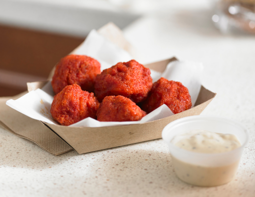 Breaded honey sriracha boneless wings in to-go tray with side of creamy sauce  