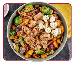 Overhead view of a bowl of roasted vegetables, chicken chunks, cheese and whole pecans