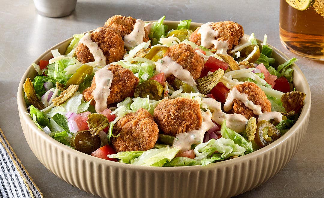 Salad bowl with breaded beef bites, diced tomatoes, jalapeños and cheese on a bed of lettuce with a drizzle of dressing