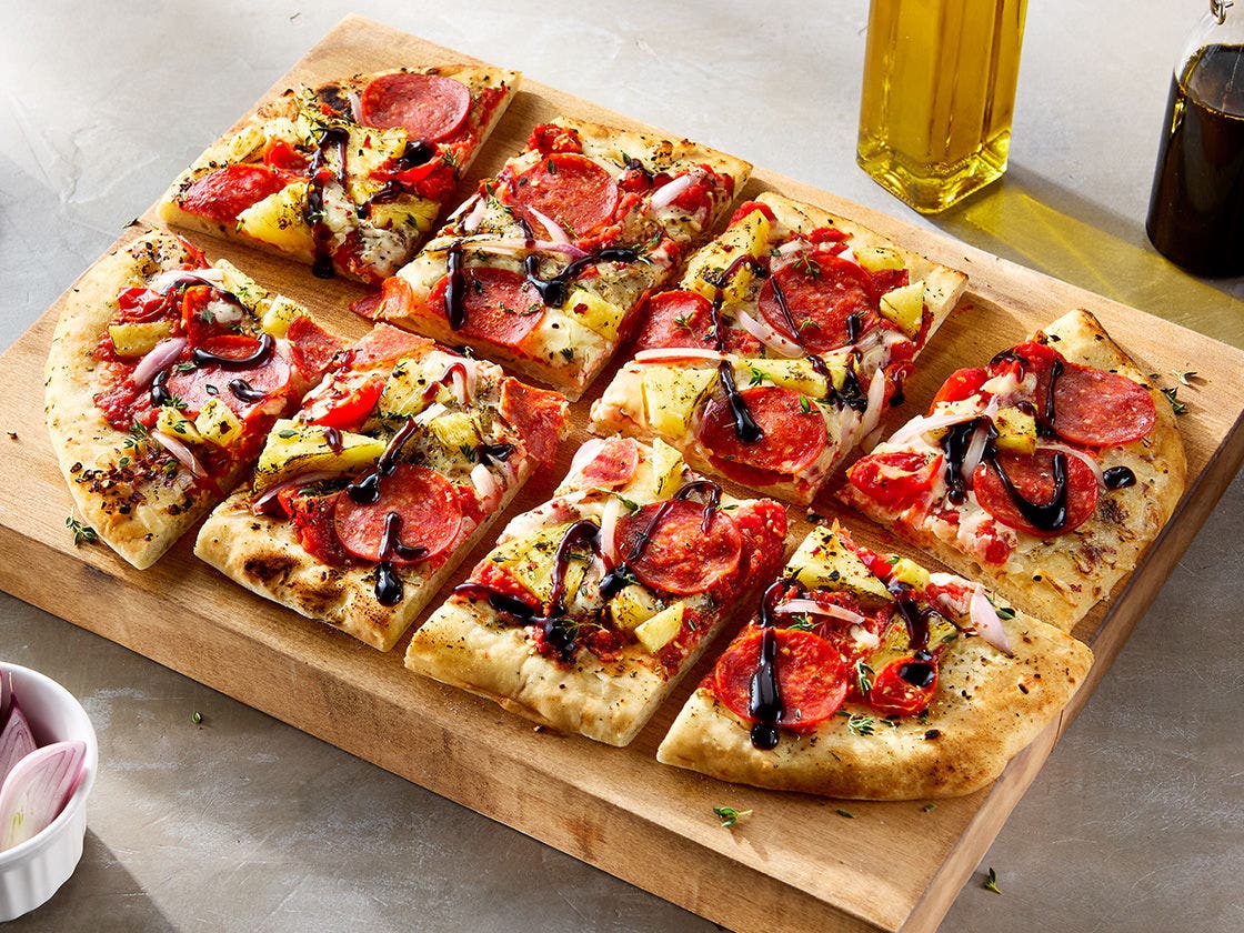 Square-cut pizza with pepperoni, pineapple, balsamic-roasted cherry tomatoes, smoked provolone, shallot slices, thyme, and balsamic glaze drizzle.