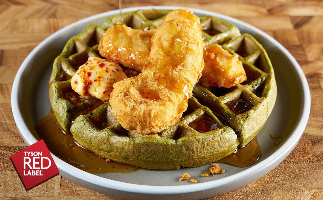 A gray plate with waffle topped with crispy chicken, butter and maple syrup 