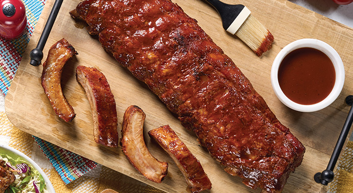 Baby back ribs on a cutting board with a side of BBQ sauce
