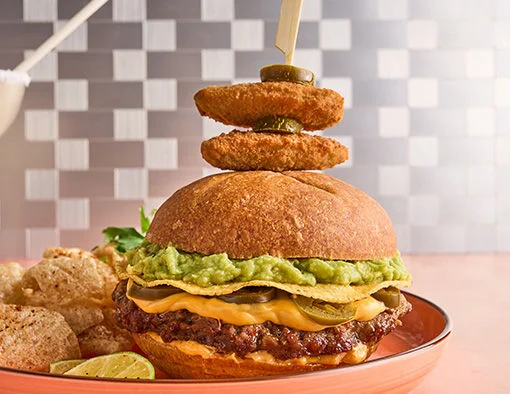 A burger with cheese, jalapeños, guacamole, and a skewer of fried jalapeños, served with pork rinds