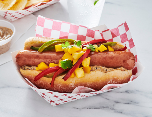Island Dog with Cheddarwurst, peppers, mango, pineapple, jerk aioli, and cilantro in a tray on marble