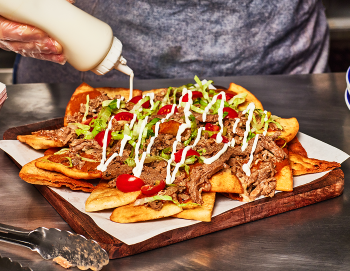 chef drizzles a sauce on a stack of shredded beef nachos with lettuce and diced tomatoes