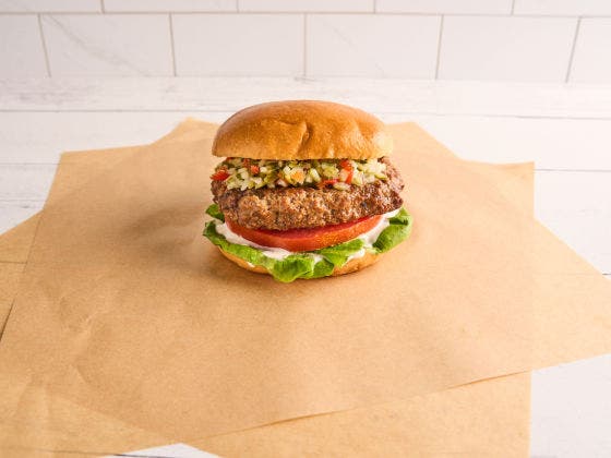 A fresh burger with lettuce, tomato, and relish on a bun, set on brown paper