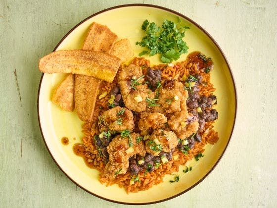 A plate of fried chicken over rice and beans with fried plantains and cilantro