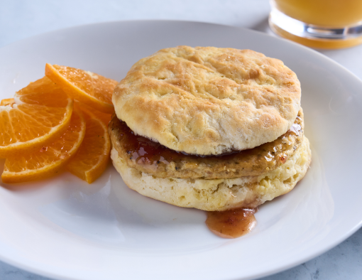 A plate with a biscuit stuffed with a sausage patty, jam and chipotle peppers served with orange slices 