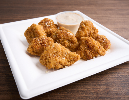 Plate of breaded boneless chicken wings dusted with parmesan served with ramekin of cream sauce 