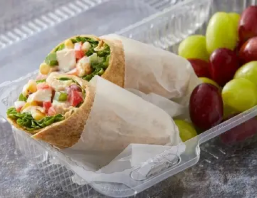 To-go box of grilled chopped chicken, corn, diced peppers, onions and cheese sauce in a halved tortilla  