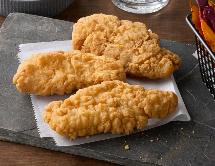 Three homestyle chicken tender fritters resting on parchment paper atop a dark slate board