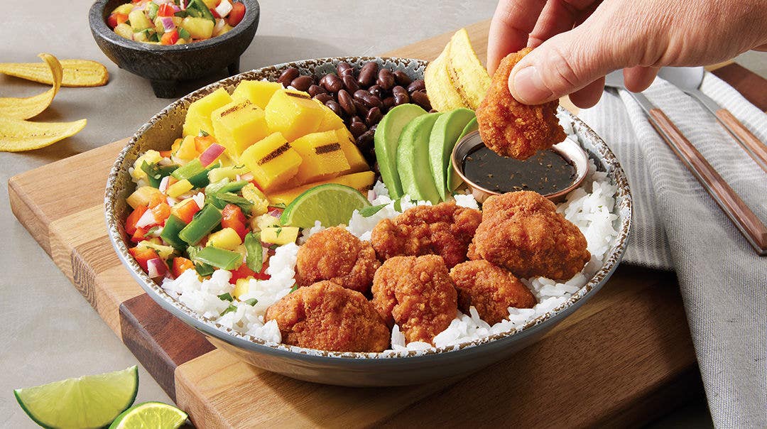 hand dipping chicken breast chunk fritters into dipping sauce 