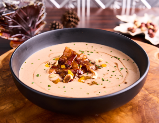 Creamy soup with bacon, nuts, and herbs in a black bowl on a wooden surface with autumn decor