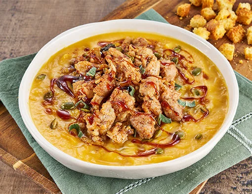 Creamy roasted sweet potato chowder topped with maple-glazed pulled chicken, herb-buttered cornbread croutons, pepitas, and crispy fried sage