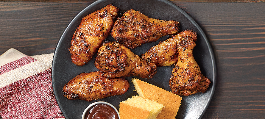 Plate of sweet heat smoked chicken wings on a dark platter with barbecue sauce and a piece of cornbread, set on a rustic wooden table