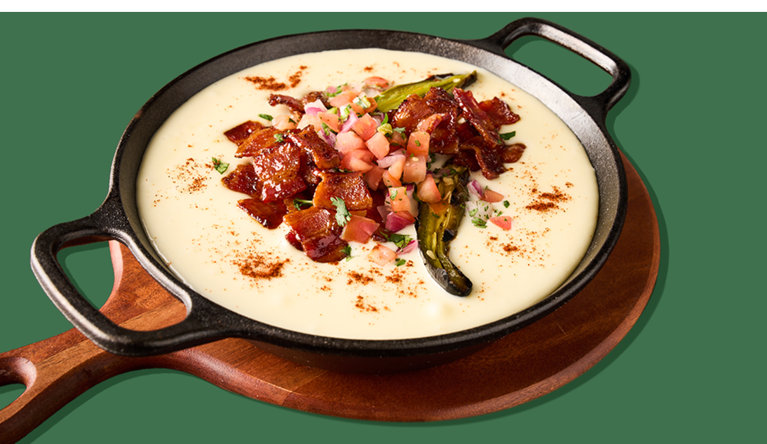 Overhead view of creamy queso dip loaded with bacon, pico de gallo, and jalapeños