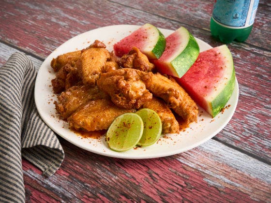Chicken wings with tamarind glaze, served with chili lime watermelon and lime wedges on a white plate