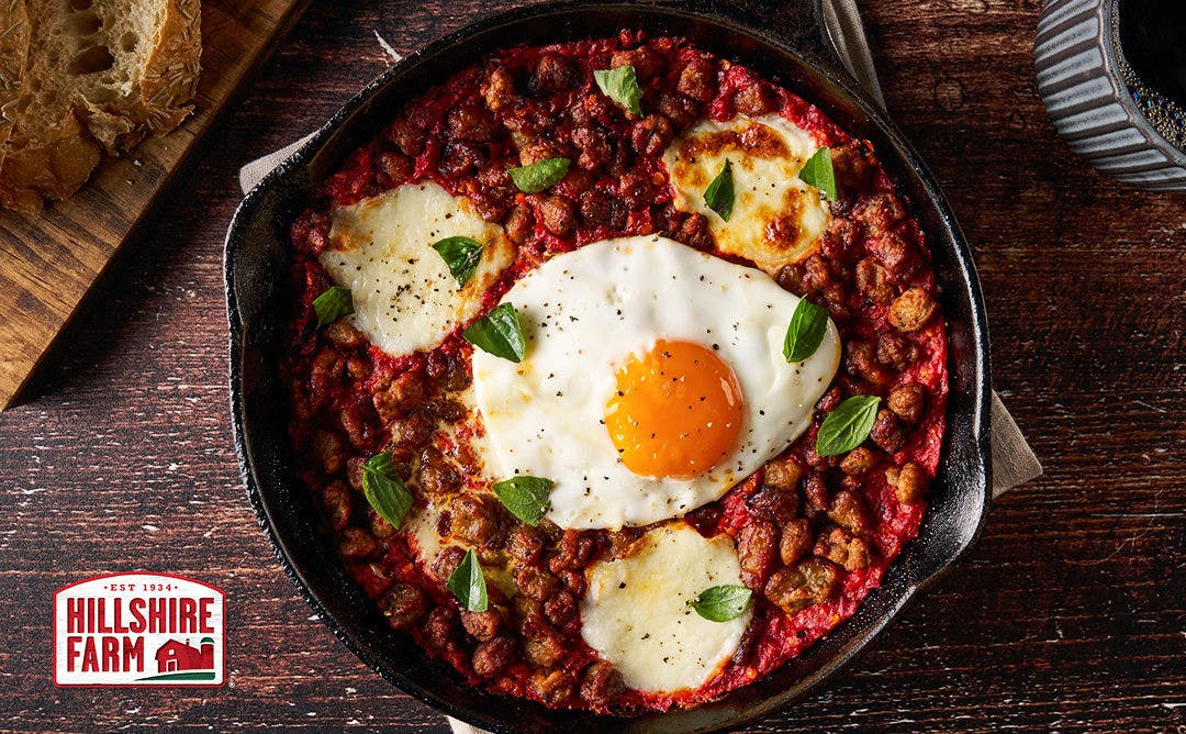 A small cast-iron skillet with a sausage-filled tomato sauce topped with a sunny-side-up egg and melted cheese 