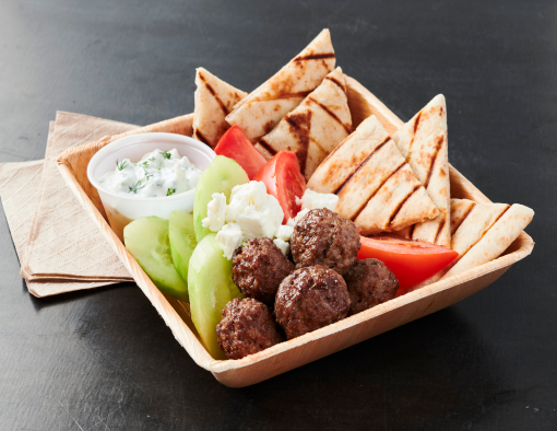 Beef meatballs in a bowl with pita wedges, sliced cucumber feta cheese, tomato wedges and ramekin of tzatziki sauce 