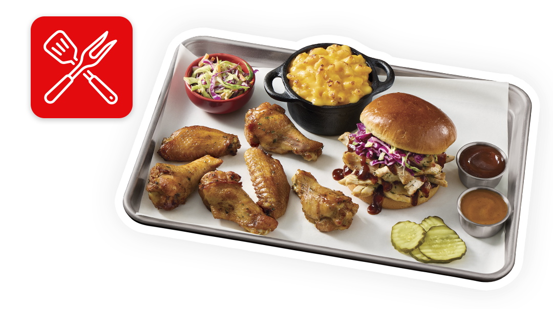 Tray with glazed chicken wings, pulled BBQ sandwich with slaw, mac and cheese, pickles, sauces, and coleslaw on white background