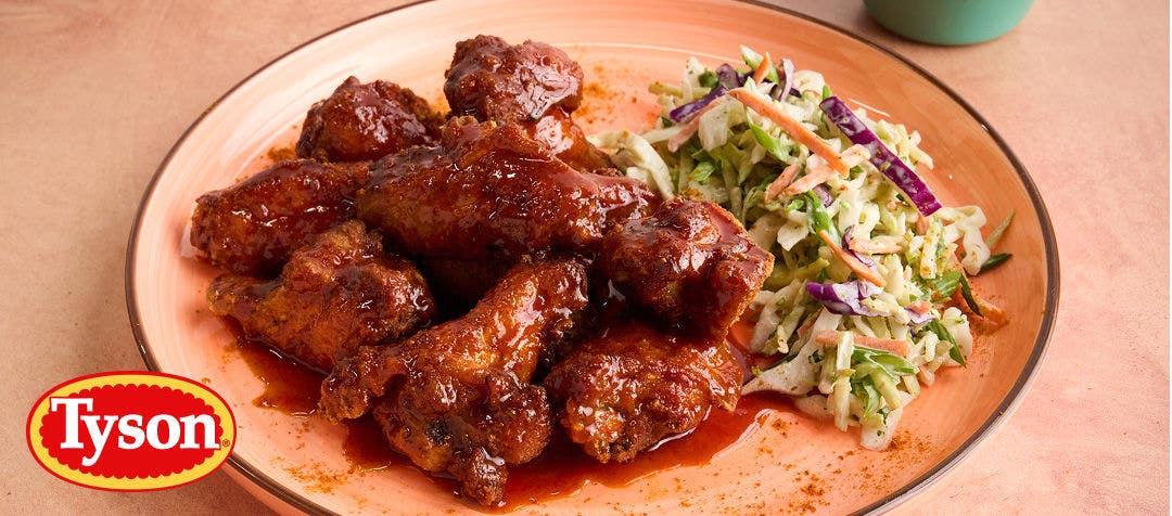 A closeup view of chicken wings in a dark red sauce on a light red plate with a side of slaw     