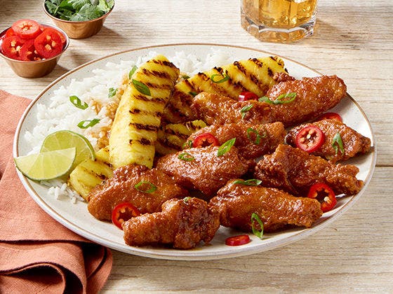 Bone-in chicken wings in Pineapple Tamarind glaze on a plate with grilled pineapple and white rice, all topped with slices of Fresno pepper and scallion greens.