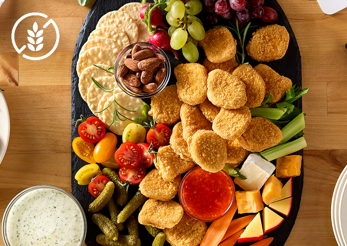Crispy gluten-free chicken nuggets on a board with fresh vegetables, fresh fruit, gluten free crackers and sauces on the side