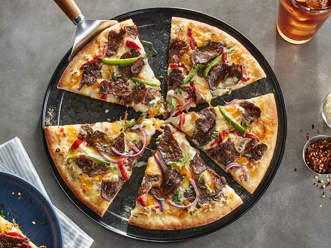 Philly cheesesteak pizza topped with sliced beef, garlic white sauce, peppers and onions