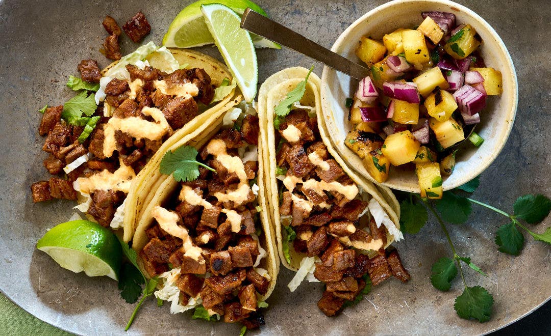 three beef tacos on a silver plate with a side dish of pineapple pico de gallo