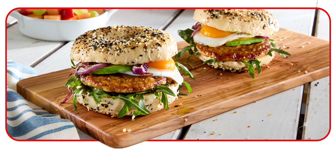 Two egg and sausage bagels sitting on a cutting board