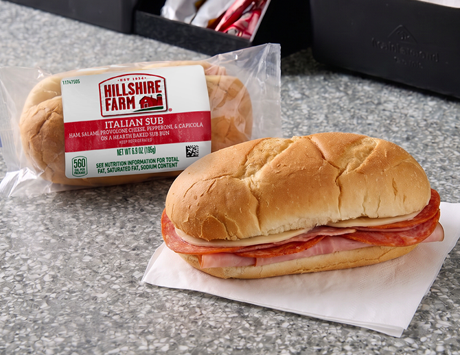 Two Italian sub sandwiches, one in a clear wrapper and the other setting on a napkin  