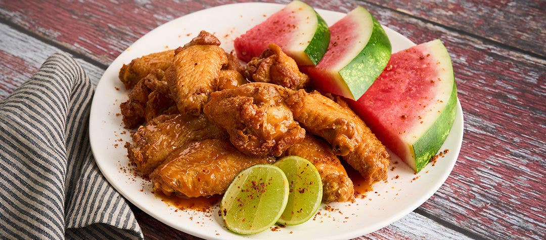 A plate of crispy, unbreaded wings on a white plate garnished with watermelon wedges and sliced lime      