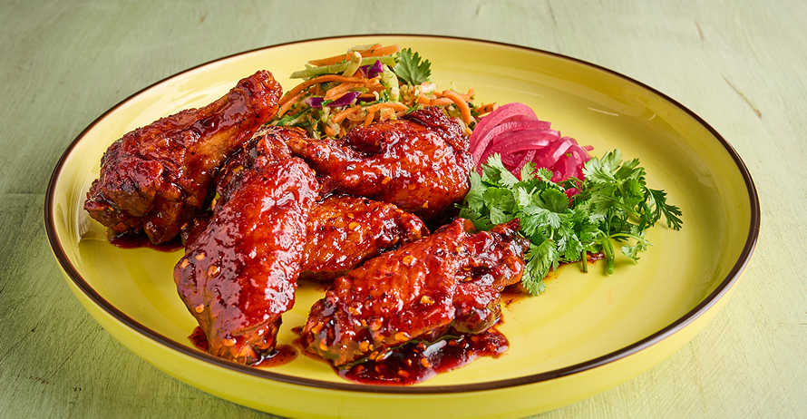 Red-sauced chicken wings on a yellow plate with coleslaw, pickled red onions, and cilantro