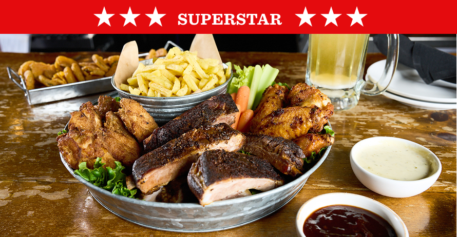 A large metal platter of barbecue with ribs, chicken wings, fries, celery, and carrots