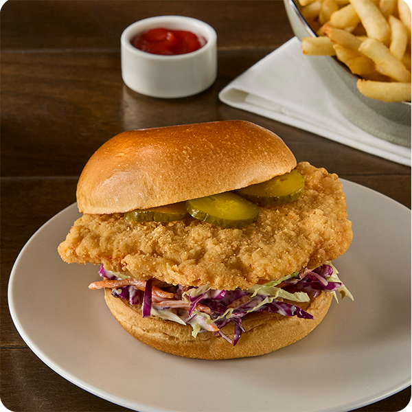 Crispy chicken breast sandwich with pickles and slaw on a bun, served with fries.