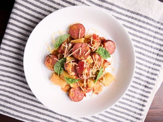 Rigatoni with sausage, tomato-bacon cream sauce, egg yolk, basil, and Pecorino Romano on a white plate
