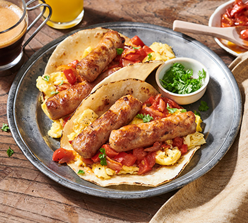 Breakfast tacos with scrambled eggs, sausage, tomatoes, and herbs on a rustic plate.