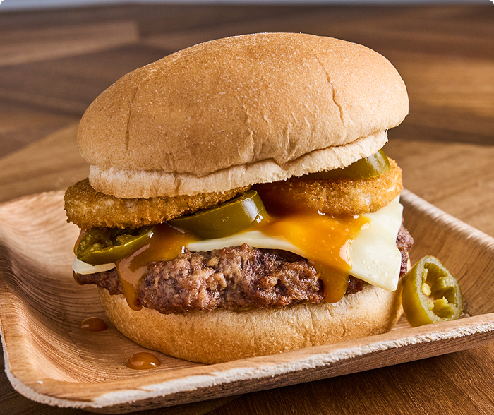 Grilled beef burger with smoky barbecue sauce, melted American cheese, jalapeños and onion rings on a white wheat bun