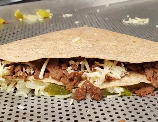Folded tortilla with exposed filling of sliced steak, mayo, roasted vegetables and shredded cheese on flat grill 