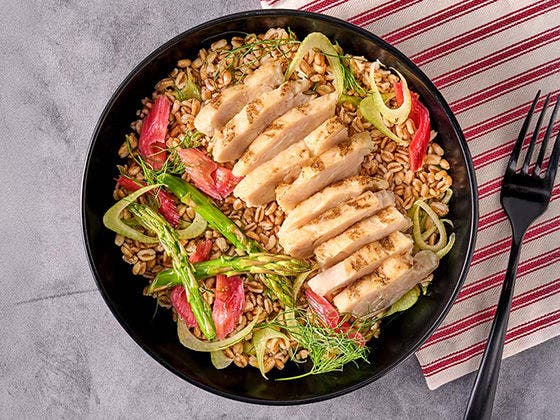 Bowl of chilled farro, shaved fennel, pickled rhubarb, asparagus and dill in lemon vinaigrette, topped with Grilled Chicken Breast Strips