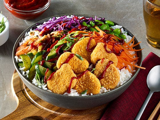 Sticky rice base in a bowl  topped with kimchi, pickled cucmber, gluten free chicken breast nuggets and a fried egg.