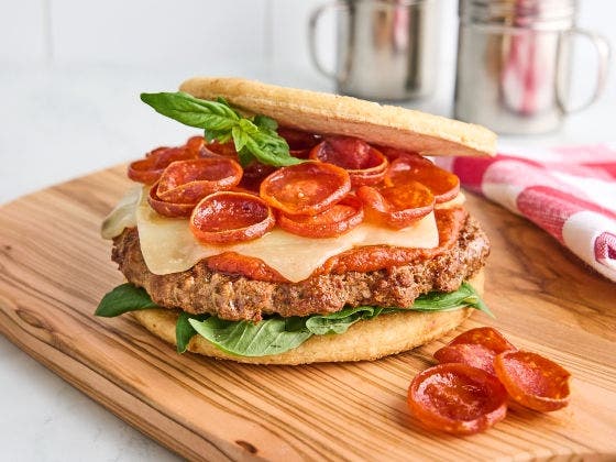 Pizza burger with beef patty, cheese, pepperoni, basil, and pizza dough buns on a wooden board