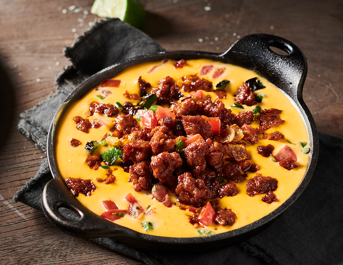 Cast-iron serving skillet filled with rich cheese dip, crumbled chorizo and diced tomatoes and peppers