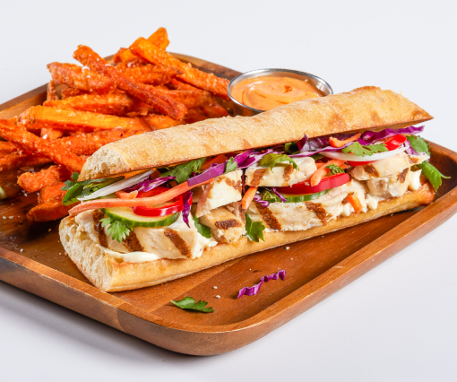 Sandwich made with grilled chicken breast strips on a wooden board with a side of fries