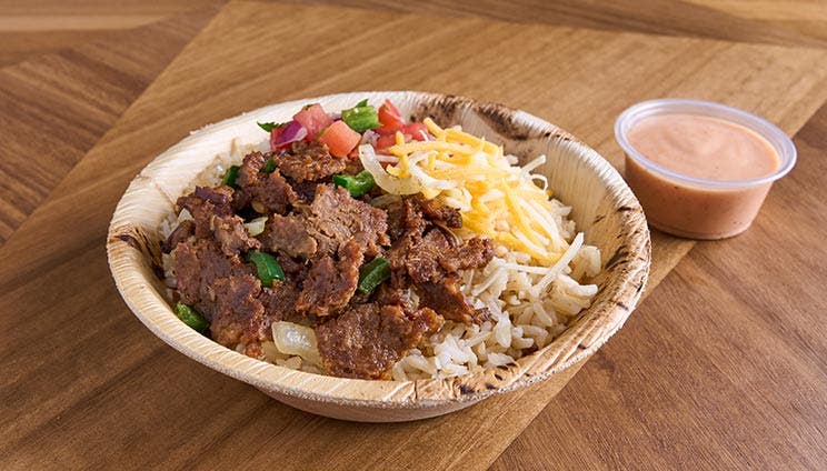 Steak burrito bowl with rice, cheese, pico de gallo, and chipotle sauce in an eco-friendly bowl