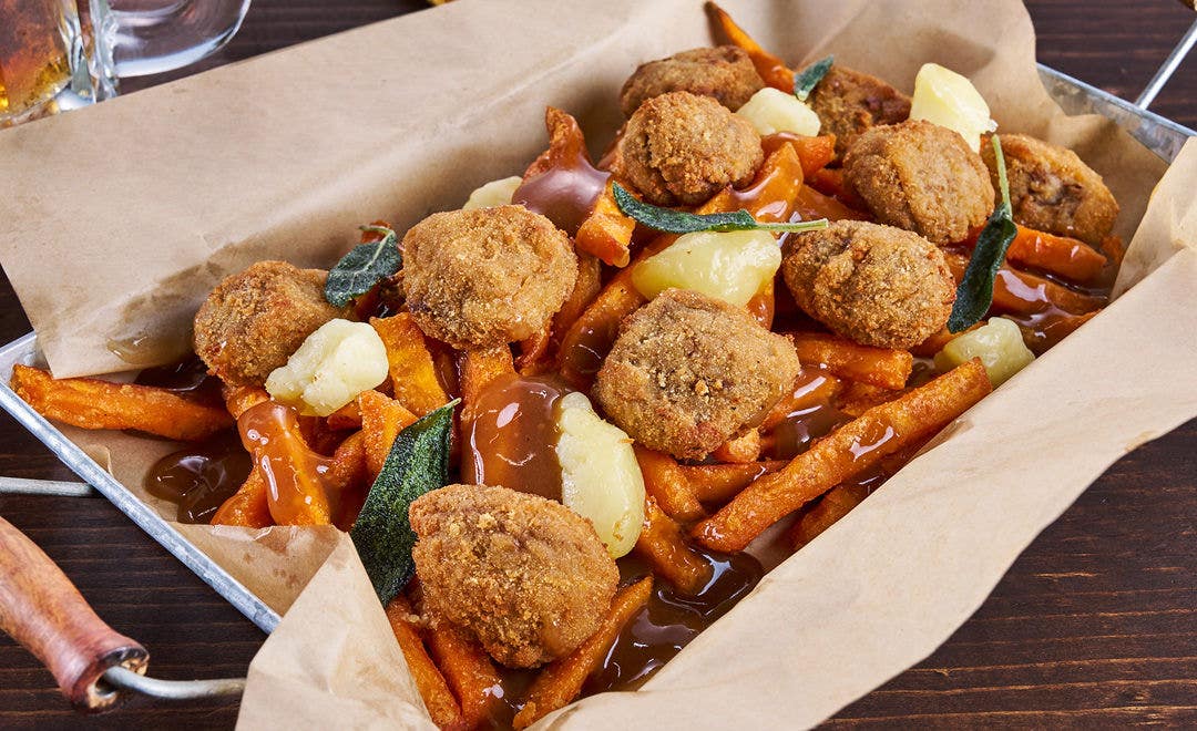 A paper-lined tray with sweet potato fries, breaded beef bites and cheese curds with gravy 